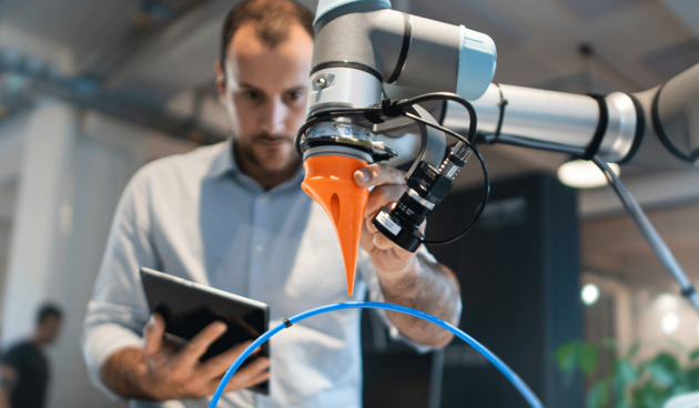Man with tablet in hand in front of a robotic arm.
